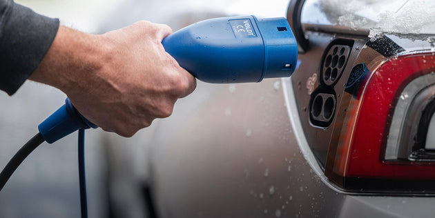 Wet hand connecting a blue Type 2 plug to the charging port of a red electric car